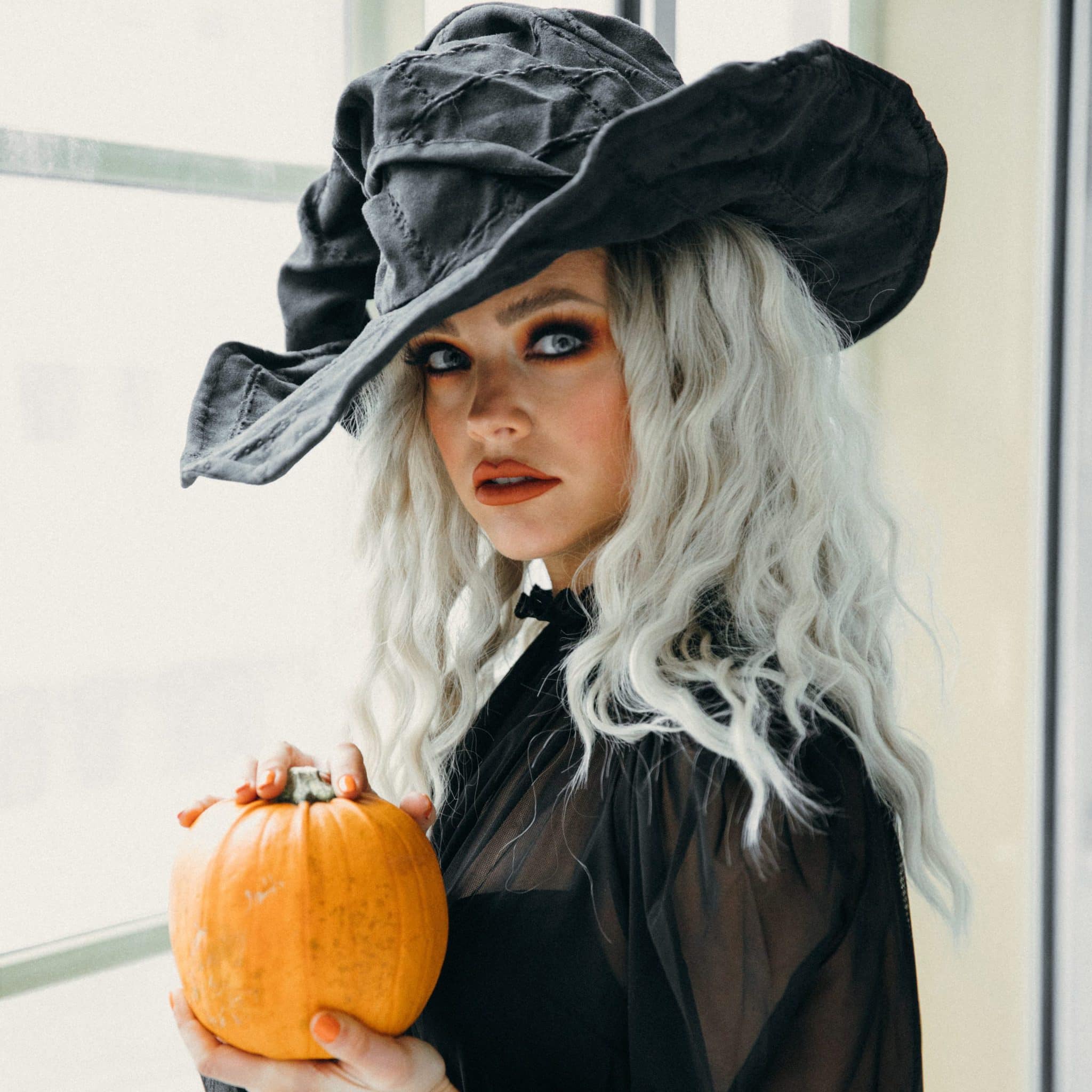 young girl dressed as a witch with silver hair, holding a pumpkin 